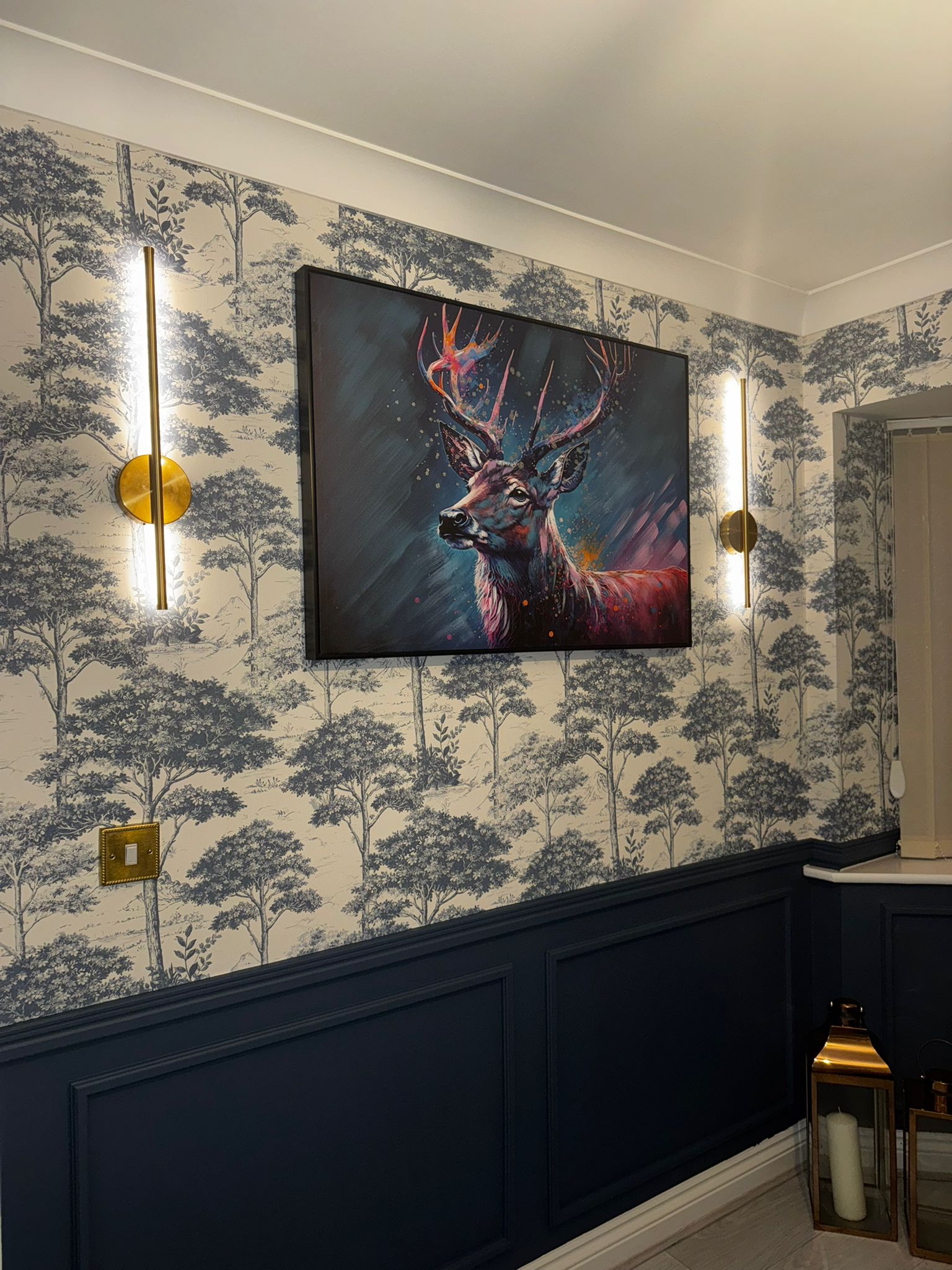 Study interior with toile wallpaper, deep blue wainscoting and brass wall sconces flanking statement artwork